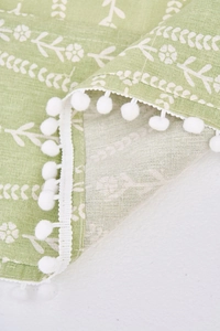 Detalle de la funda antipolvo verde hierba con estampado floral y borde de pompones
