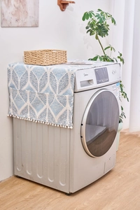 Détail de la housse de lave-linge à motifs géométriques avec pompons blancs et poches de côté