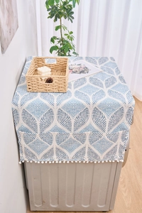 Détail de la housse anti-poussière avec motifs feuilles bleues, poches et bord à pompons