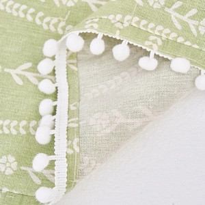 Funda antipolvo verde claro con patrón de hojas y pompones blancos decorativos