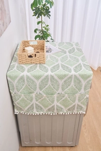 Détail de la housse anti-poussière à motif de feuilles vertes avec pompons et poches de côté