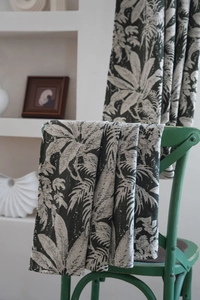 Detail of tropical palm leaf jacquard fabric draped on a vintage green chair in a room
