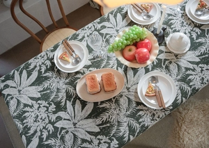 Top view of dark green tablecloth with white palm leaf pattern and dining setting