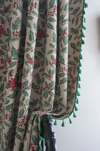 Detailed view of jacquard curtain fabric with holly leaf patterns and green fringes