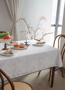 Detail of off-white jacquard tablecloth featuring floral patterns and brown scalloped edges