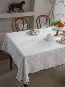 Detail of white jacquard tablecloth with elegant floral patterns and dark brown scalloped edges