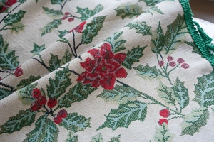 Detailed jacquard fabric showing festive holly leaves and red berry patterns with green fringe