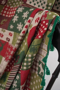Detail of Christmas throw blanket with reindeer patterns and green fringe tassels