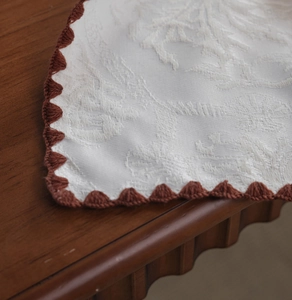 Macro shot of white floral jacquard fabric with dark reddish-brown crochet scalloped edges