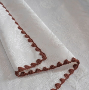 Macro shot of white jacquard tablecloth fabric with brown crochet scalloped edges