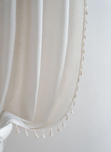 Close-up of cream white jacquard curtain with damask patterns and elegant fringe tassels