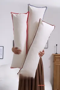 Close-up of long lumbar pillows with colored pom-poms and delicate embroidered wavy edges