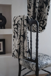 Detail of black tropical leaf jacquard fabric draped on a vintage wooden chair