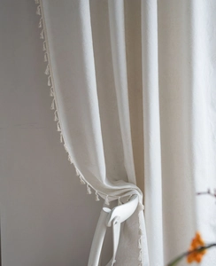 Detail of cream white jacquard curtain fabric with decorative tassels and texture