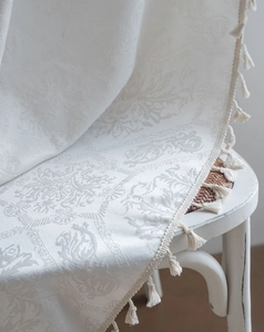 Close-up of vintage floral jacquard fabric with elegant tassel fringe in creamy white