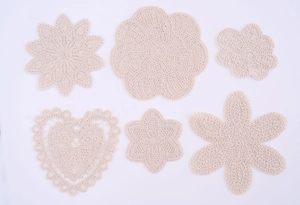 Detail showing various hand-crocheted beige cotton coasters in diverse floral shapes