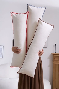 Detailed view of three long cream throw pillows with colorful pom-pom wave trim