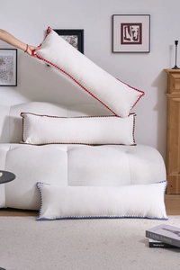 Detail of a long cream throw pillow featuring decorative multi-colored pom-poms on the edge