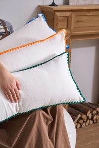 Detail of white cotton pillows with vibrant wavy embroidered edges in colorful finishes