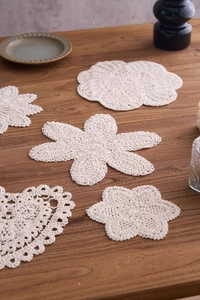 Detailed close-up of ivory hand-crocheted cotton coasters in various shapes on wood table