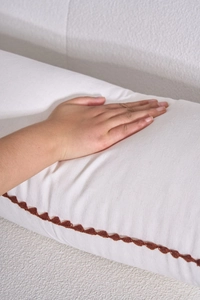Detail of white lumbar pillow showing textured fabric and brown wavy braided edge trim