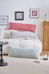 Détail de coussins lombaires tissés géométriques avec de longues franges sur un canapé blanc