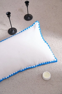 Detailed view of white rectangular pillow with elegant blue crochet lace wavy edges