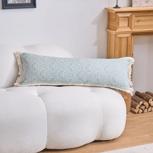 Dettaglio di un cuscino jacquard blu con nappe bianche su un divano di peluche