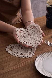 Detailed close-up of ivory crochet heart-shaped cotton coasters on a wooden table