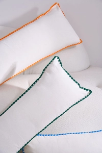 Detail of white cotton lumbar pillow with colorful crochet scalloped edges on white sofa