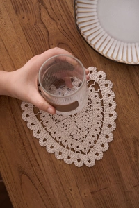Macro shot of handmade beige cotton heart-shaped crochet coaster on a rustic wood surface