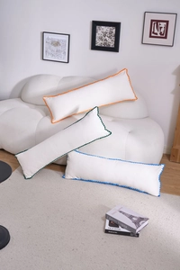 Detailed view of white embroidered long pillows with colorful pom-pom edges on a sofa