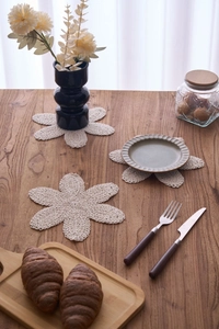 Drei beige handgehäkelte Baumwolluntersetzer in Blütenform auf einem Holztisch