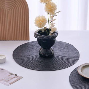 Detailed top view of dark grey round woven placemats on a clean white dining table setup