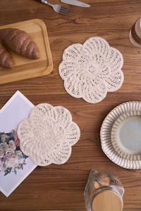 Macro detail of a beige hand-crocheted floral cotton coaster on a warm wooden tabletop