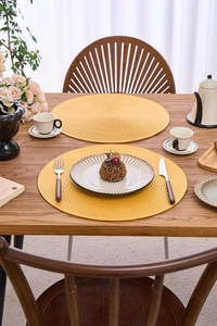 Detail of round yellow woven placemats on a wooden table with afternoon tea set