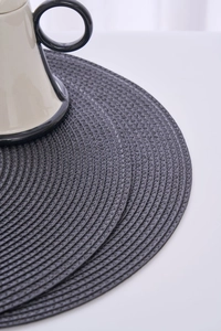 Detail of round dark grey woven placemats with white stitching and ceramic mug set