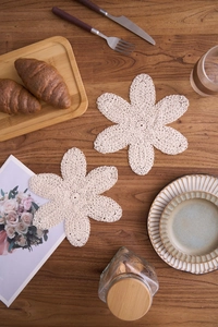 Handgefertigter gehäkelter Baumwoll-Untersetzer in Blumenform auf dunklem Holztisch