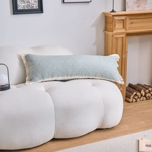 Sage green lumbar pillow with geometric weave and tassels on white sherpa sofa