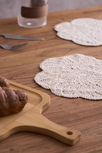 Close-up of handmade crochet cotton coaster with petal shape and hollow design on wood