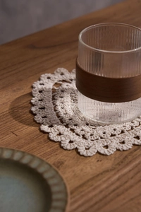 Detail of hand-crocheted beige cotton coaster with lace edge and ribbed glass cup