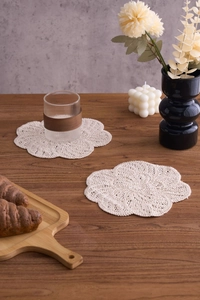 Detail view of two handmade cream cotton crochet coasters on a rustic wooden table