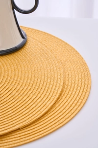 Detail of round ginger yellow woven placemat showing spiral texture and fine sewing