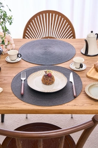 Close-up of a 38cm dark grey woven round placemat with spiral texture on a wooden table