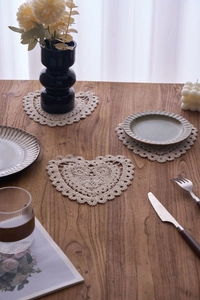 Macro detail of a heart-shaped cotton crochet coaster with hollow patterns on a wood table