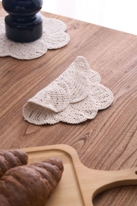 Detail of handmade off-white crochet cotton coaster with petal edges on a wooden table