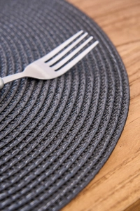Close-up of a round dark gray woven placemat with a fork on a wooden table surface