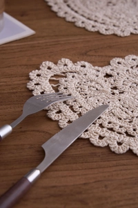 Close-up of handmade cream crochet lace coaster with scalloped edges on dark wood