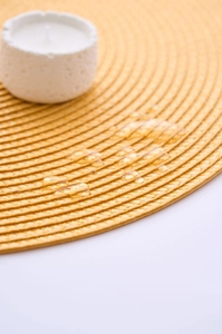 Detail of round yellow woven placemat featuring a waterproof surface with water droplets