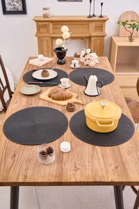 Detailed macro view of four round black braided PP placemats set on a wooden dining table